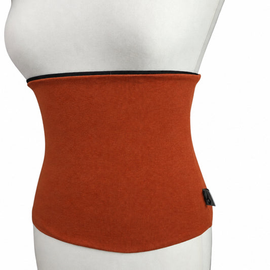An orange waist trainer or waist cincher worn by a white mannequin torso, set against a white brick wall background.