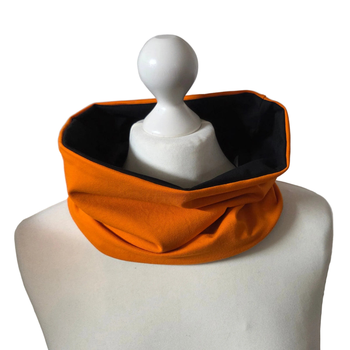 An orange neck warmer or gaiter with a black interior lining, displayed on a white mannequin torso against a plain white background.