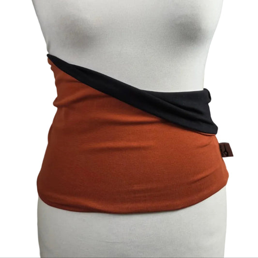 An orange wrap skirt with a black diagonal sash detail, displayed on a white mannequin torso against a white brick wall background.